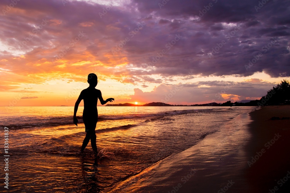 Silhouette of boy walking on the beach at sunset