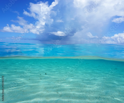 Half and half, Pacific ocean seascape, shallow sandy seabed underwater with cloudy blue sky over the water, French Polynesia 