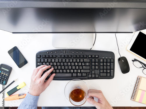 Top view of male hands working on computer and holding tea cup on the table