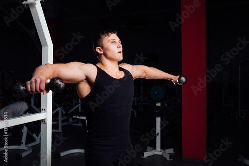 Portrait of a muscular young man lifting weights on gym