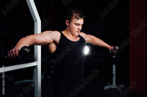 Portrait of a muscular young man lifting weights on gym background. Exercise the shoulders