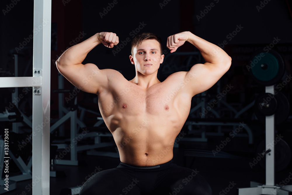 professional fitness bodybuilder sitting on the bench and demonstrates muscles of your body after a workout, at gym. professional fitness bodybuilder sitting on the bench and demonstrates muscles of your body after a workout, at gym.