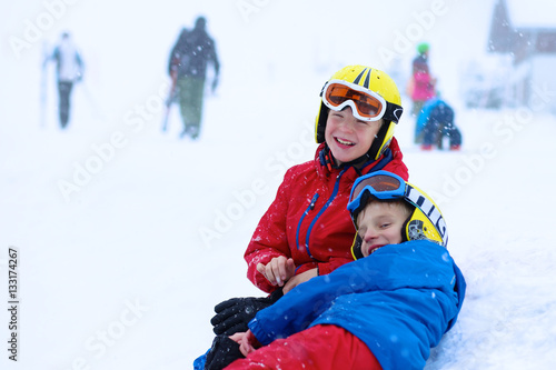 Two happy school boys, twin brothers in colorful snowsuits, having fun skiing in alpine mountains during snowy winter vacation