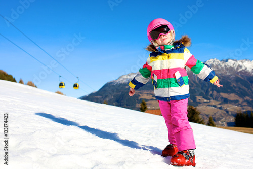 Happy child enjoying winter vacation in Alpine resort in Austria. Little girl playing in the snow. Active sportive toddler learning to ski.