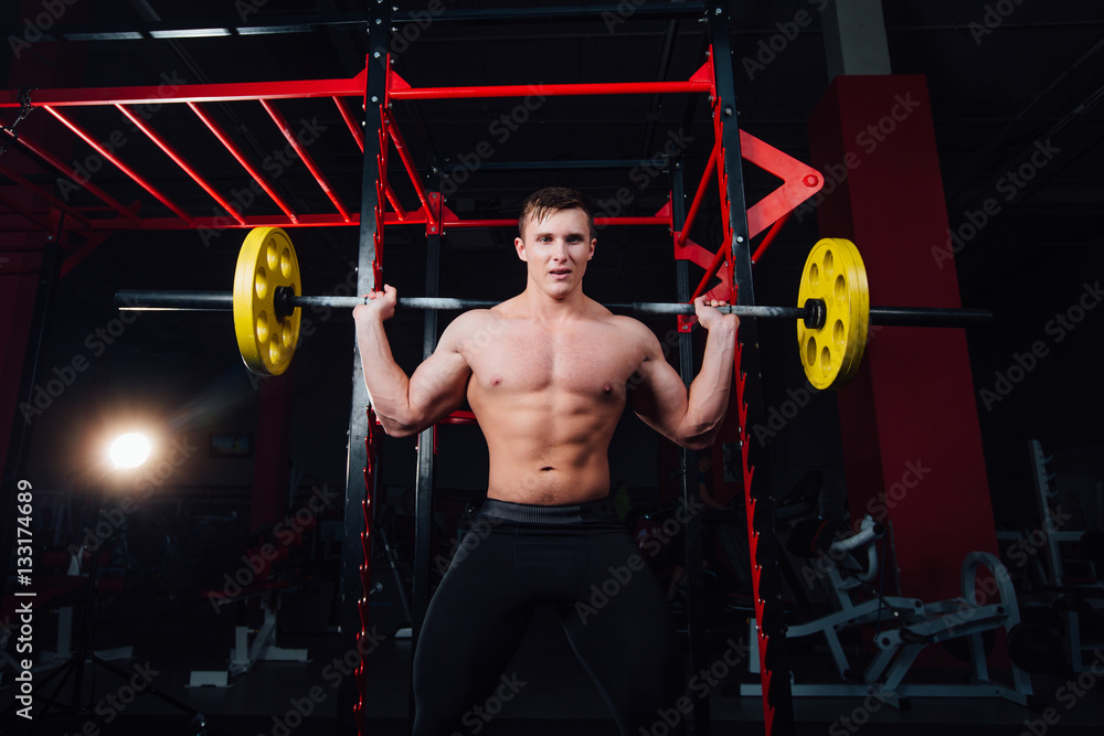 portrait of a handsome athlete at gym. man does the exercise with barbell, standing and squatting. big confident portrait of a handsome athlete at gym. man does the exercise with barbell, standing and squatting. big confident