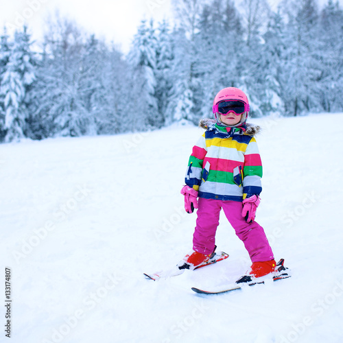 Happy child enjoying vacation in Alpine resort in Austria. Little girl skiing in mountains. Active sportive toddler wearing helmet and glasses learning to ski. Winter sport for family.