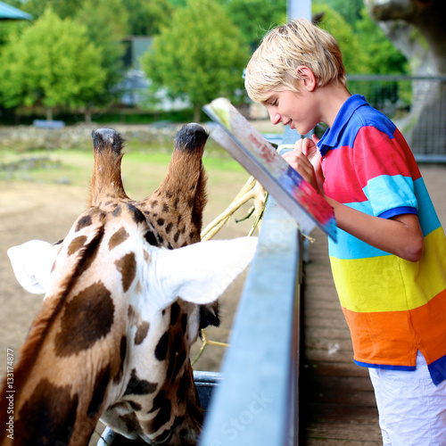 Happy school boy enjoying family day at the zoo. Child watching and feeding giraffe. Kid having fun at animals safari park.
