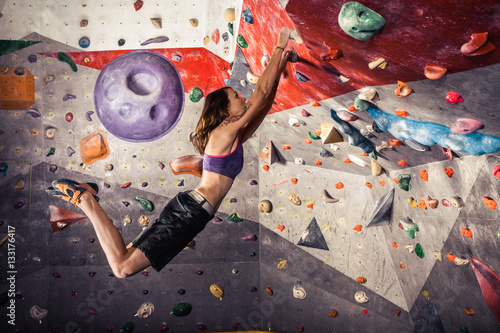 young woman climbing artificial boulder indoors photo