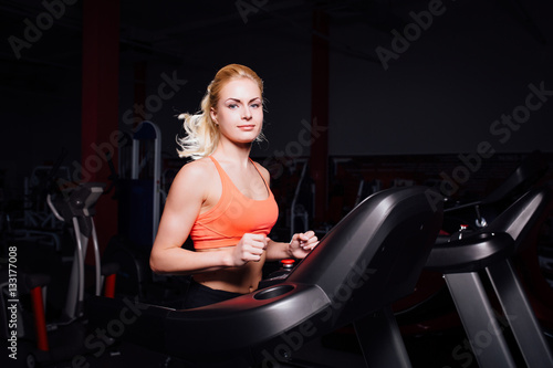 Young beautiful cute girl in fitness model in the gym running on the treadmill with bottle