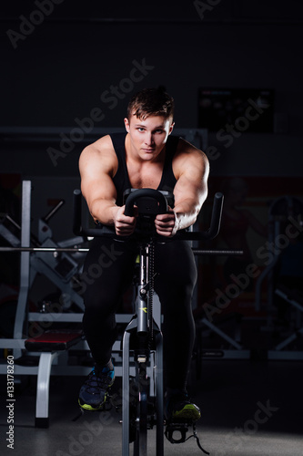 Portrait of a handsome man workout on fitness the exercise bike dark at gym.