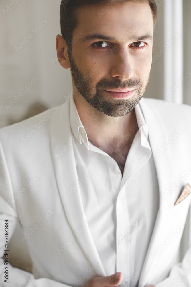Elegant young handsome man with a beard in a white classic suit. Elegant young handsome man with a beard in a white classic suit.