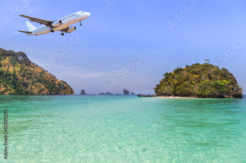      passenger airplane landing above small island in blue sea  on blue sky background. travel destinations concept. 