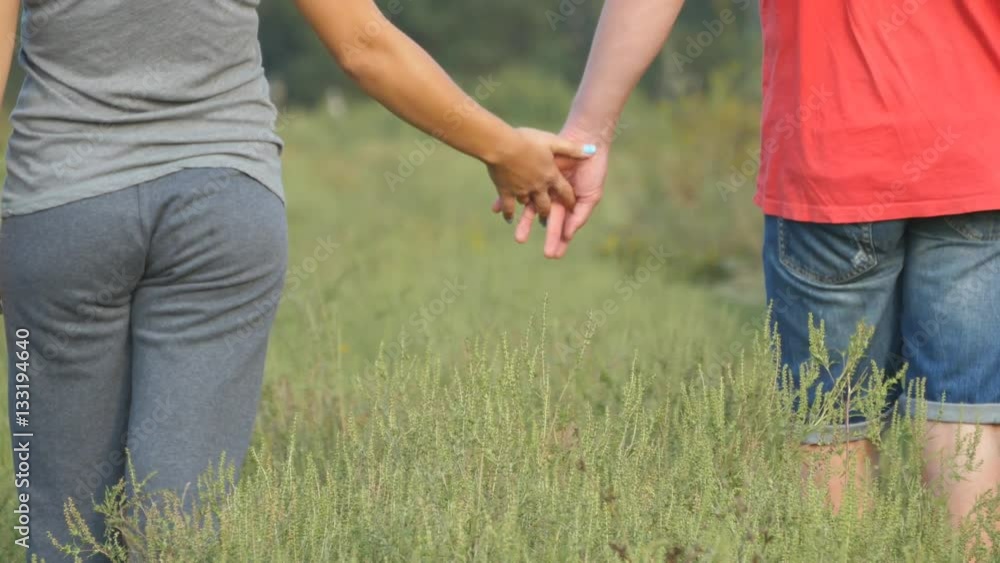 Young couple joining hands outdoor. Man and woman taking arms on nature background. Male and female hands comforting and stroking each other. Symbol of love and devotion. Romantic outside. Close up Young couple joining hands outdoor. Man and woman taking arms on nature background. Male and female hands comforting and stroking each other. Symbol of love and devotion. Romantic outside. Close up
