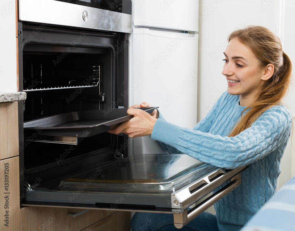 female putting baking tray in kitchen oven foto de Stock Adobe Stock