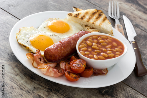 Traditional full English breakfast with fried eggs, sausages, beans, mushrooms, grilled tomatoes and bacon on wooden background
 photo