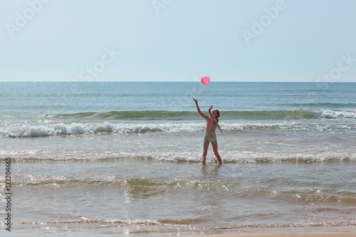 Girl with a red ball in the sea among the waves