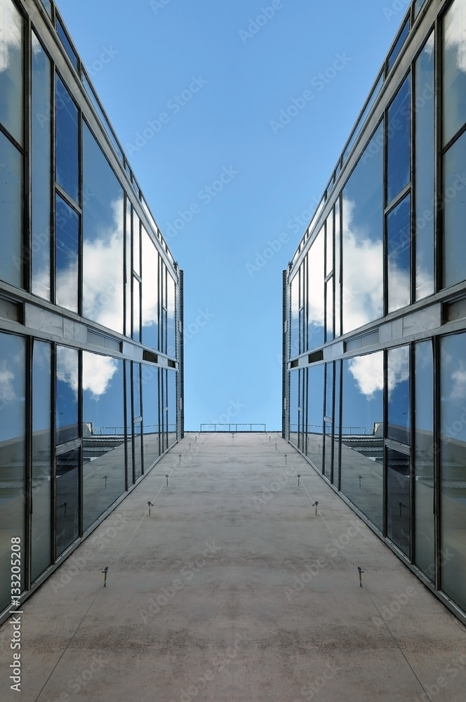Fototapeta premium Looking up at the facade of a modern building with glass mirror walls against the blue sky. Symmetrical vertical view.