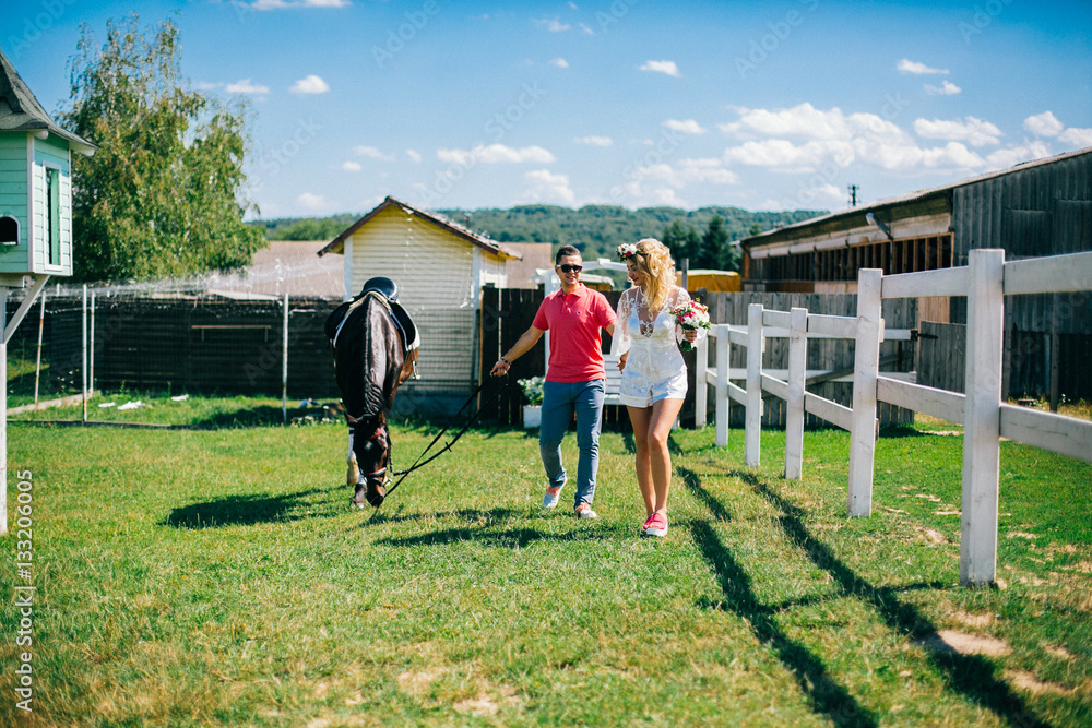 Young couple stay and walking near black horse at green farm