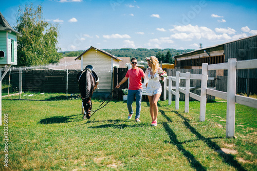 Obraz na płótnie Young couple stay and walking near black horse at green farm w salonie