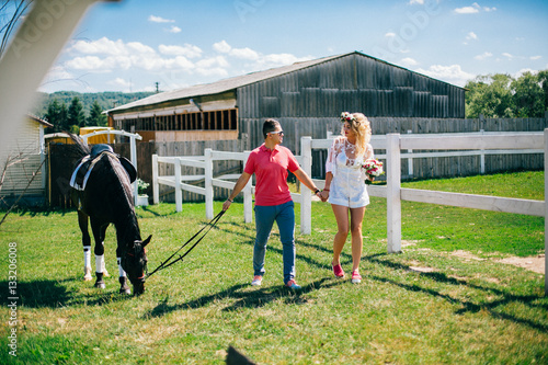 Young couple stay and walking near black horse at green farm