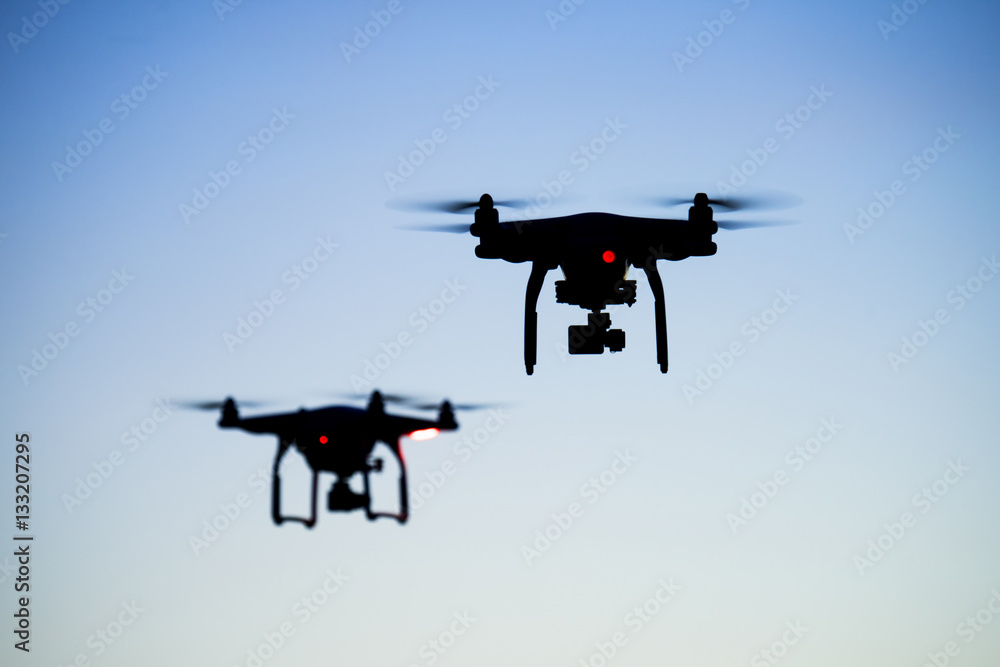 Two drones silhouette flying under the clear sky background Two drones silhouette flying under the clear sky background