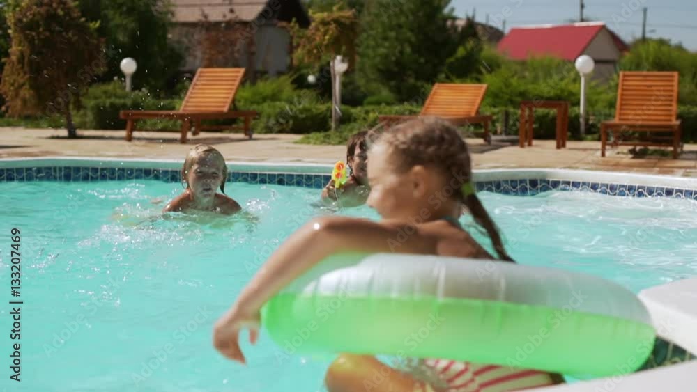 Two girls with inflatable tube shooting from water guns at two boys in pool with in slowmotion Two girls with inflatable tube shooting from water guns at two boys in pool with in slowmotion