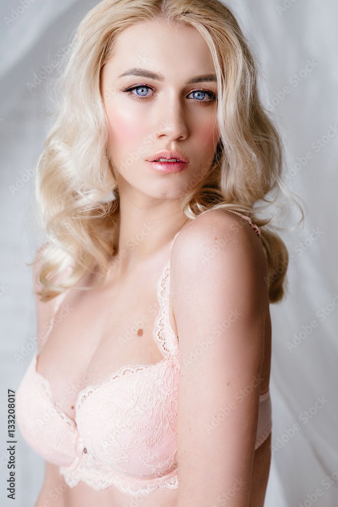 Beautiful blonde girl in light pink lingerie posing on a white