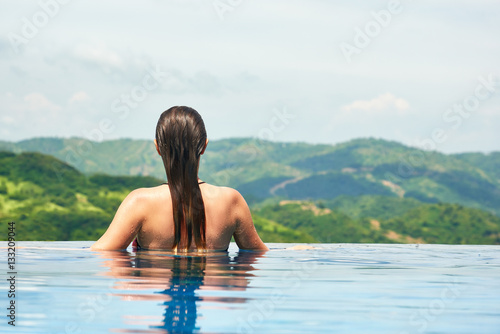 Young sexy woman enjoying resting on the edge of outdoor swimmin