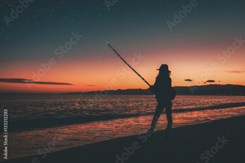 Silhouette of a girl while she is fishing with the fishing rod at the susnet