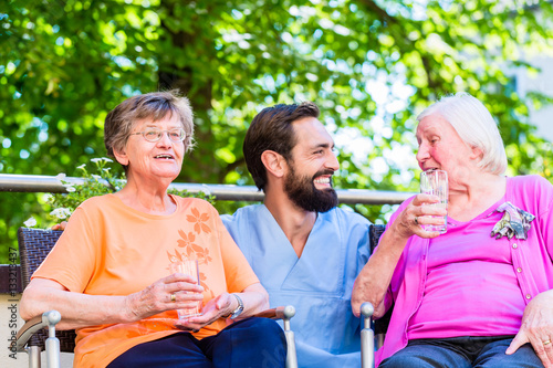 Altenpfleger trinkt Kaffee mit Seniorinnen auf der Terrasse