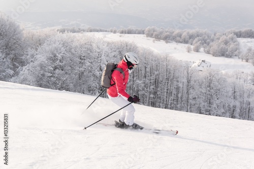 Woman skier running downhill on snow piste in mountain ski resort 