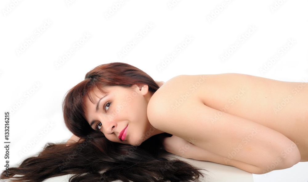 Young long-haired nude brunette lying on white table on a white background Young long-haired nude brunette lying on white table on a white background