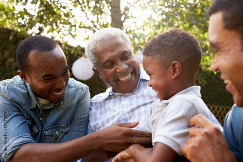 Black grandfather, sons and grandson talking in a garden photo
