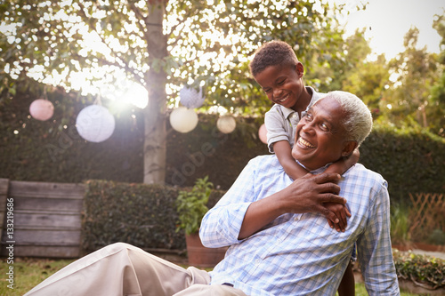 Young black boy embracing grandfather sitting in garden photo