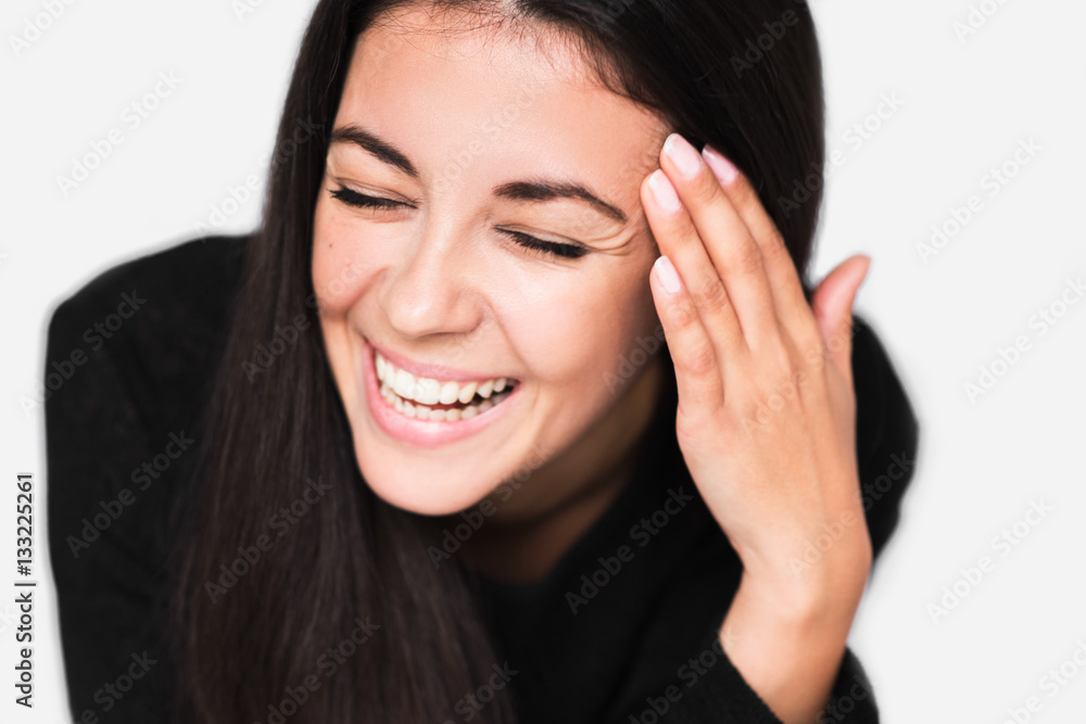 Close up portrait of cheerful woman with healthy toothy smile, with hand on temple with closed eyes. Young happy woman wearing black sweater on light grey background. Positive and happiness mood. Close up portrait of cheerful woman with healthy toothy smile, with hand on temple with closed eyes. Young happy woman wearing black sweater on light grey background. Positive and happiness mood.