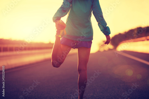 young fitness woman runner stretching legs on city road