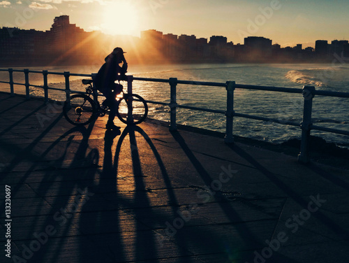 Fotografi A cyclist gazing at the sea horizon while a sunset
