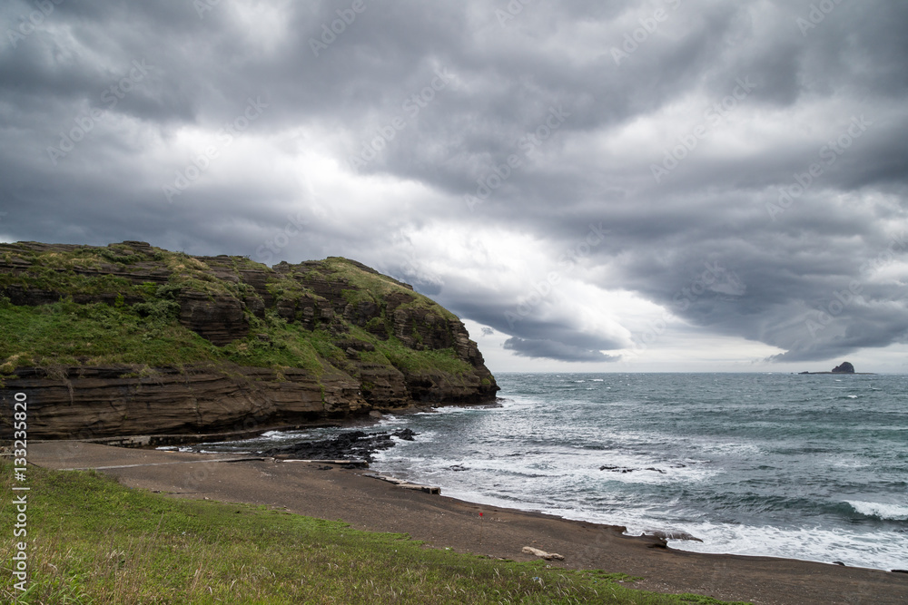 Empty beach, cliff and dramatic, dark clouds at the Yongmeori Coast on Jeju Island in South Korea.