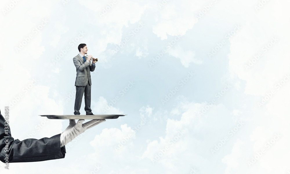 Businessman on metal tray playing fife against blue sky background Businessman on metal tray playing fife against blue sky background