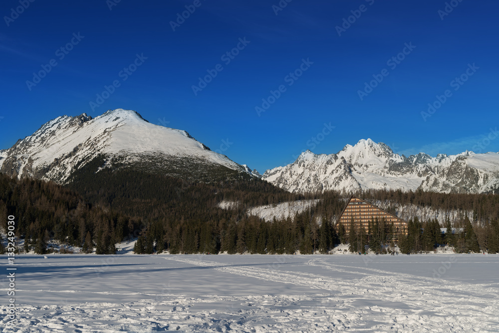 Winter view of frozen surface of Strbske Pleso (Tarn) with hotel and peaks of High Tatra mountains in background. Strbske Pleso is second largest glacial lake on the Slovak side of High Tatras.