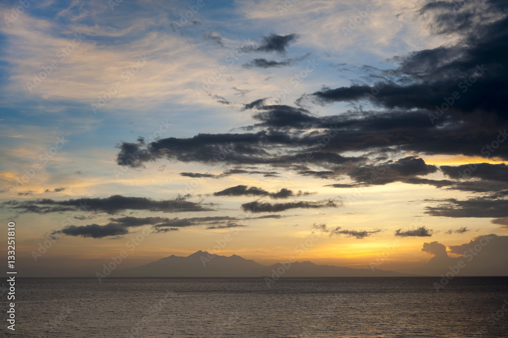 Obraz premium Sunrise Over Lombok Island, Indonesia. A dramatic sunrise over the Lombok Strait to the island of Lombok as seen from the Amed area of eastern Bali, Indonesia. Balinese fishing boats on the horizon.