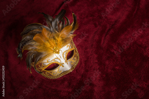 Brown golden venetian carnival mask with feathers seen from above on a draped red velvet theater curtain 