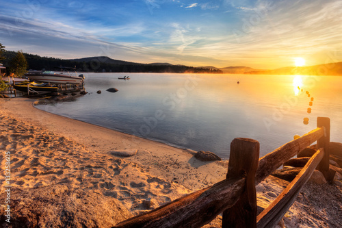 Mist rises from Merrymeeting Lake, as seen from the beach by the marina boat launch, New Durham, New Hampshire right after sunrise on a summer morning