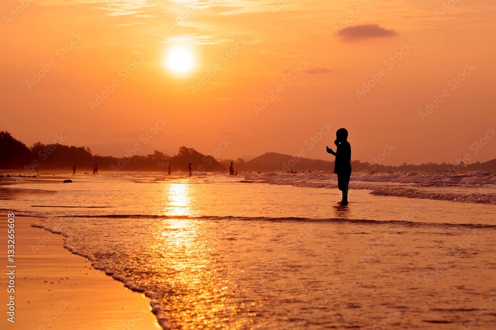 Fototapeta premium Silhouette boy standing on the beach at sunset
