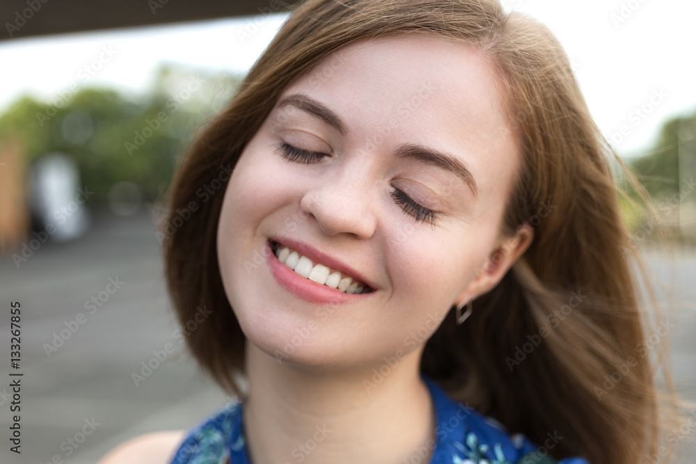 Outdoor portrait of smiling beautiful girl with bob hairstyle and closed eyes in blue top standing. Soft focus on background Outdoor portrait of smiling beautiful girl with bob hairstyle and closed eyes in blue top standing. Soft focus on background
