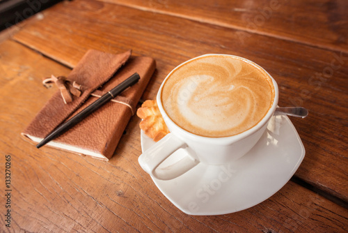 A cup of hot coffee with latte art on the surface placed in the wooden table.