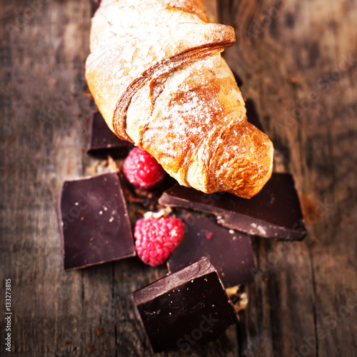 Fresh delicious croissant with chocolate  and raspberries on old photo