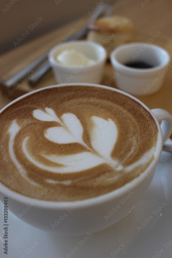 Coffee with Leaf Art with Scone in the Background Coffee with Leaf Art with Scone in the Background