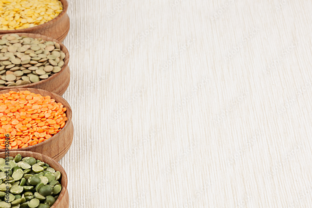Assortment of lentils in a wooden bowls with copy space on white fabric background. Top view. Healthy protein food. Assortment of lentils in a wooden bowls with copy space on white fabric background. Top view. Healthy protein food.