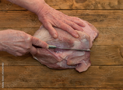 hand cuts a piece of meat, pork on a wooden table.